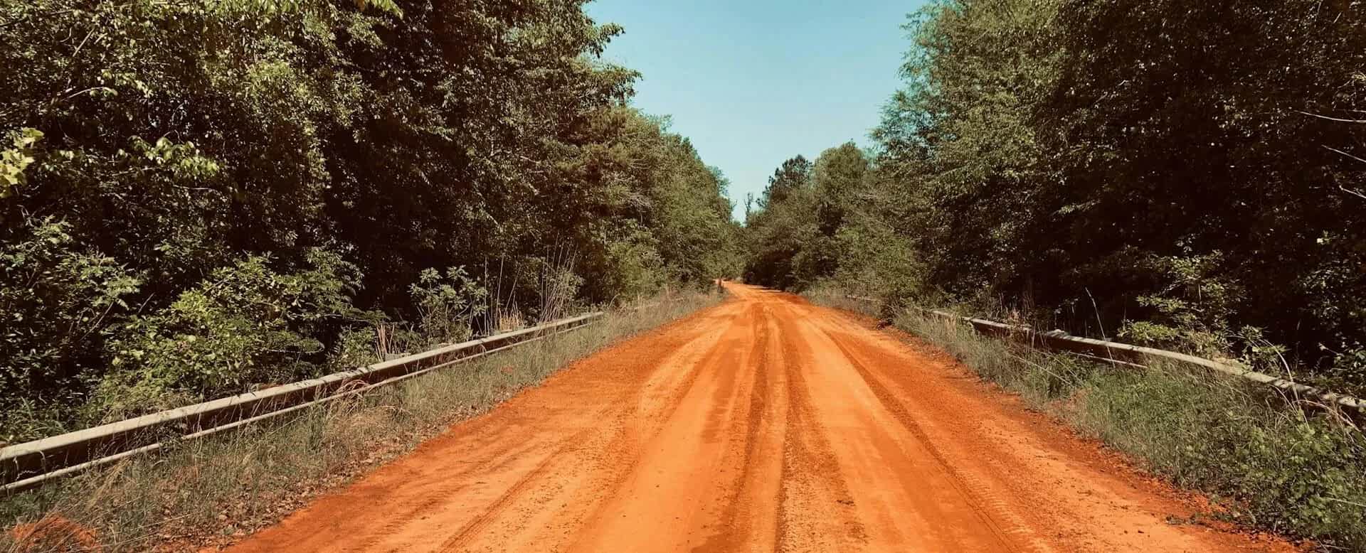 Image of a narrow red-dirt road with guard-rails